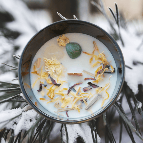 A picture of a large white candle sprinkled with Lemongrass, ginger root, rosella hibiscus flower & calendula flower and two crystals Green Aventurine and clear Quartz cimbedded in it