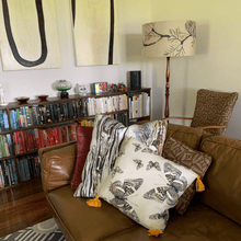 Load image into Gallery viewer, soft paperbark and butterflies in grey, yellow and beige neutrals printed on square linen designer cushions on a leather lounge with book case and contemporary Australiana decore
