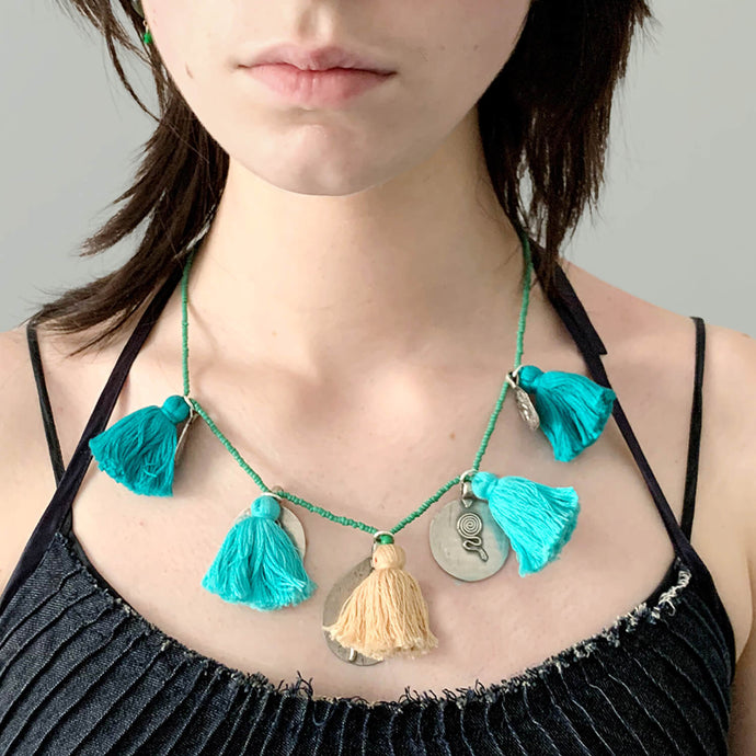 Ethically sourced Old Fashioned Online green beaded necklace with Turquoise tassels and five silver amulet charms on girl wearing blue denim