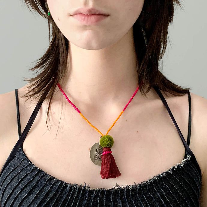 Colorful Old Fashioned Online bead necklace with tassel, pompom and silver amulet charm in pink and blue on girl close up