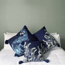 Load image into Gallery viewer, Black cockatoo and sage grevillea printed on indigo square linen designer cushion with tassels on white sheets on bed in bedroom with sage walls 

