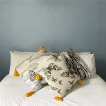 Load image into Gallery viewer, Butterfly print in grey, yellow and beige neutrals printed on square linen designer handmade cushion on  bed with white sheets in light bedroom
